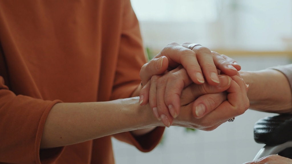 A private sitter holding the hands of an elderly woman