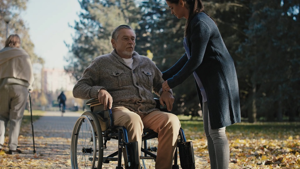 A private sitter helping a person in a wheelchair in the park