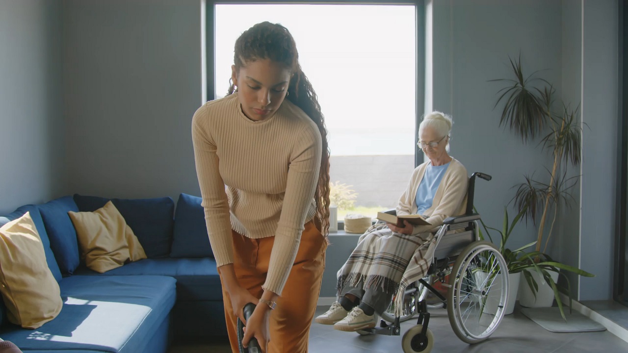 A private sitter vacuuming a room for an elderly person