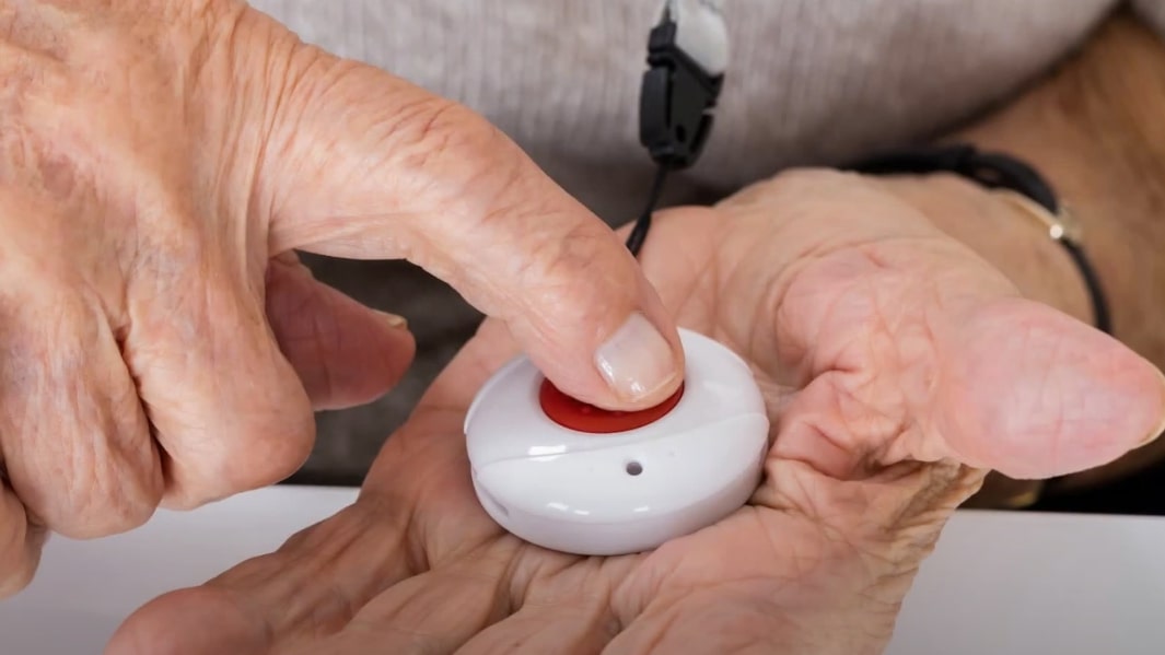 An elderly person pressing a button on a Medalerts device